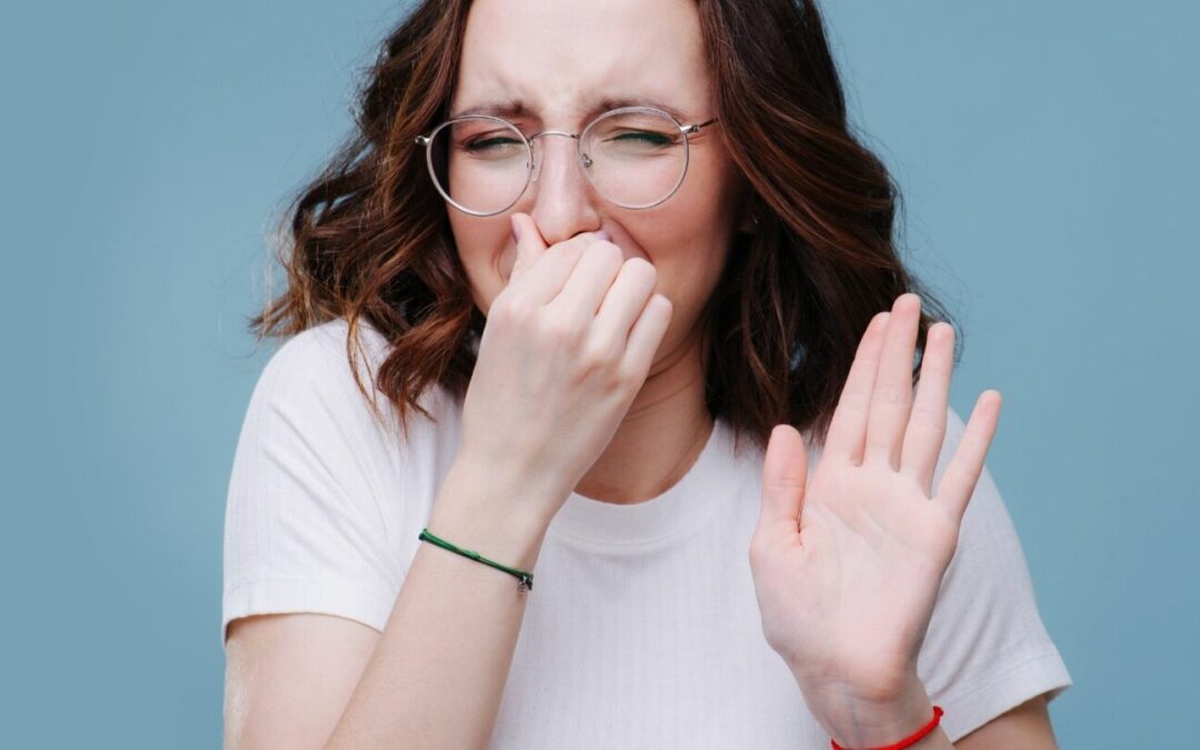 A young woman holds her nose against a bad smell, wondering how to remove odor from air ducts