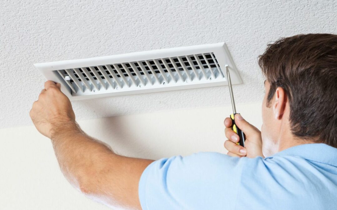 A worker unscrews an air vent to perform air duct repair